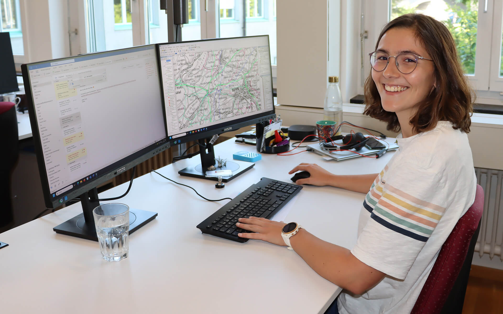 Selina Walther sitzt am Schreibtisch in ihrem Büro bei swisstopo. Auf einem Bildschirm sieht man die Schweizer Landeskarte.