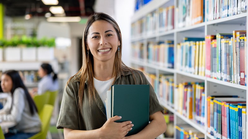 Eine junge Lehrperson steht in einer Bibliothek