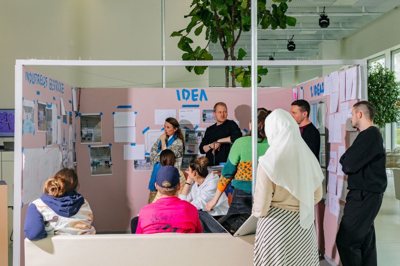 Personen stehen in einem Pavillon an der Hochschule für Gestaltung und Kunst und besprechen eine Arbeit