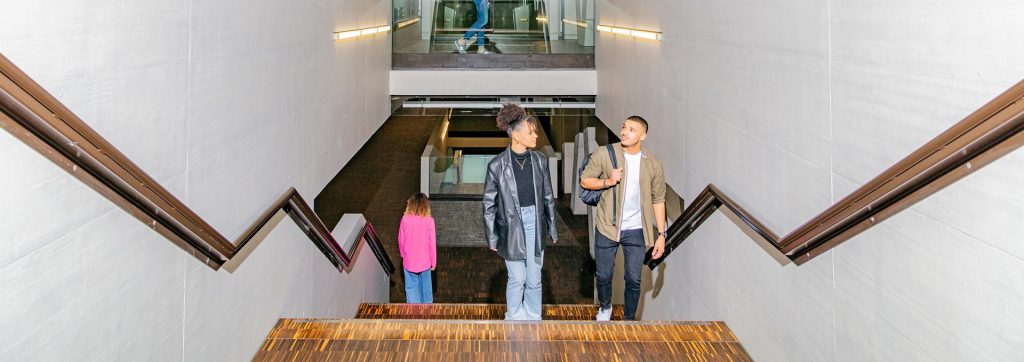 Ein junger Mann und eine junge Frau laufen die Treppe auf dem FHNW Campus Brugg Windisch hoch. Der Blick ist von oben. Die beiden schauen neugierig und zielstrebig nach oben.